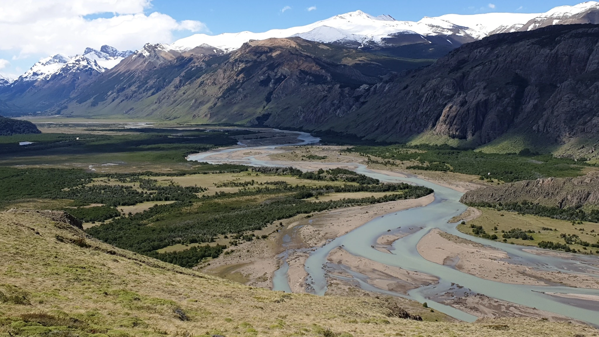 Blick über einen verzweigten, teilweise ausgetrockneten Flusslauf in einem weiten Bergtal in Patagonien